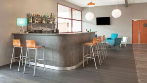 A modern bar area with a curved counter, bar stools, a television mounted on the wall, and pendant lighting.