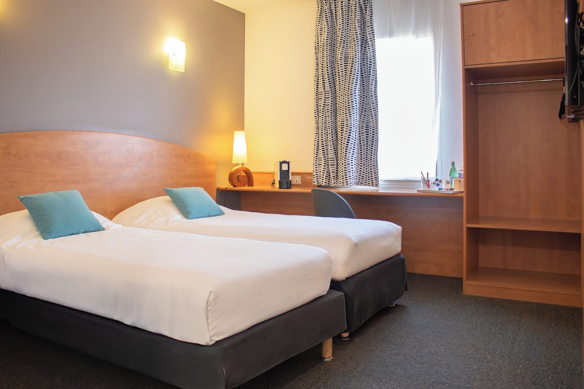 Habitación de hotel con dos camas, un escritorio, un armario y una ventana con cortinas.