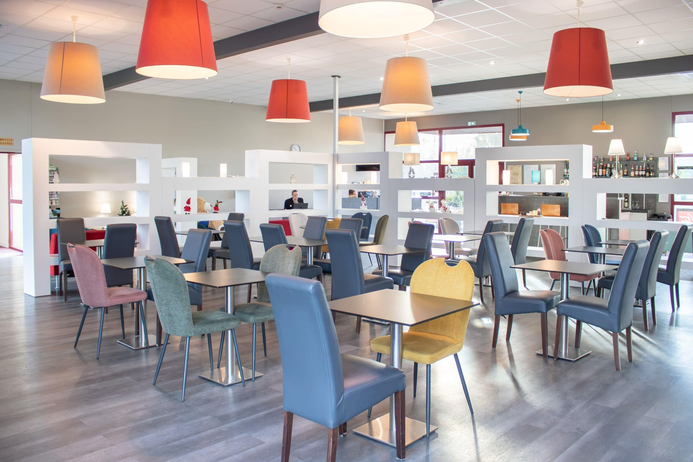 A modern dining area with multiple tables and chairs, a bar area, and a reception desk.