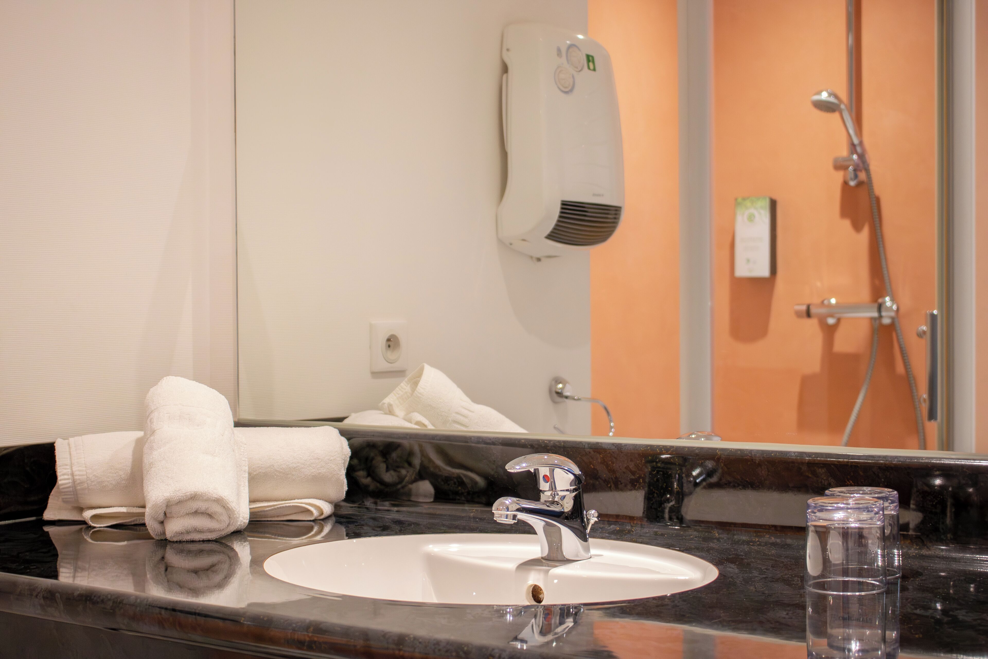 A bathroom with a sink, mirror, towel, and a handheld showerhead.