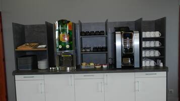 Une petite cuisine équipée d’une machine à café, d’un coin pour préparer le thé et de placards de rangement.
