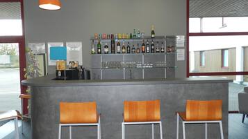 A bar area with a counter, three bar stools, and shelves stocked with bottles and glasses.