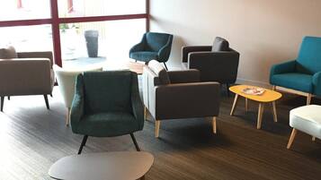 A modern lounge area with multiple seating options, including armchairs and sofas, a coffee table, and a television mounted on the wall.