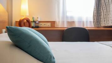 Una habitación de hotel con cama, escritorio, lámpara y ventana con cortinas.