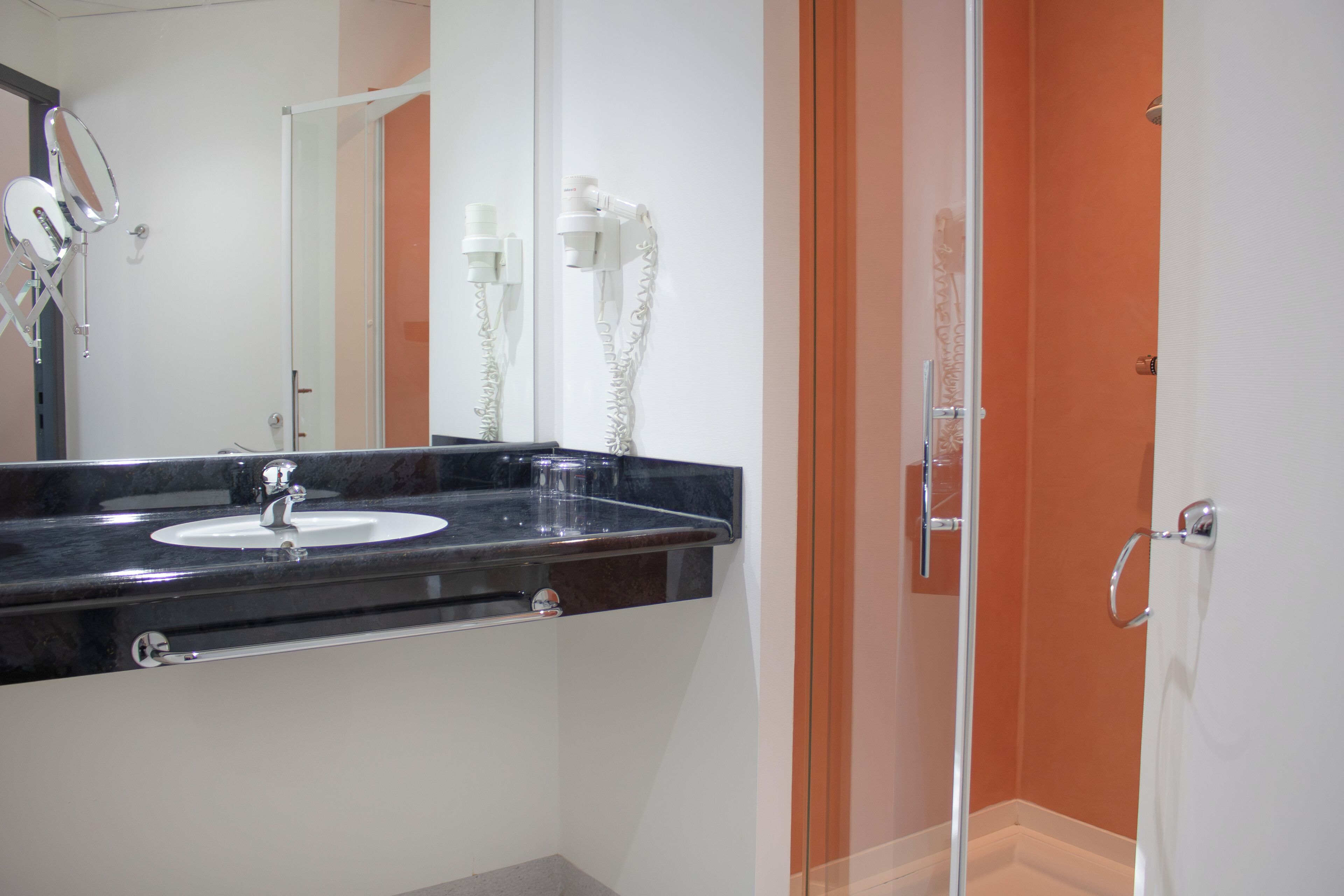 Un baño con lavamanos sobre encimera negra, espejo y cabina de ducha de cristal.