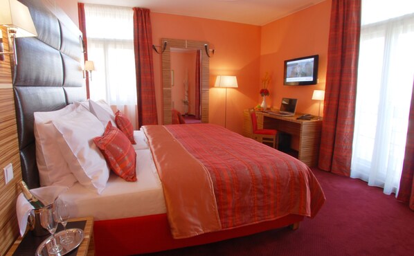 Una habitación de hotel con cama, escritorio, silla, televisor y espejo.