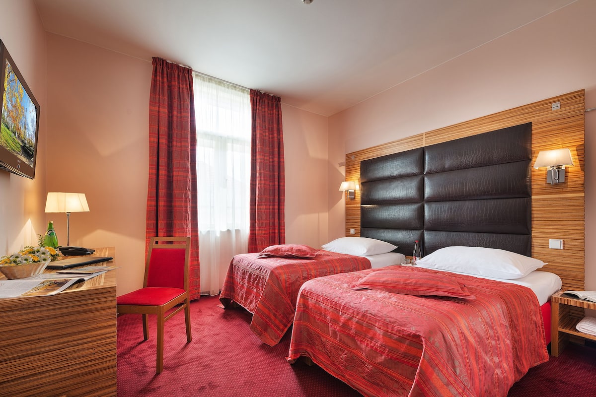 Een hotelkamer met twee bedden, een bureau met een stoel, een lamp en een schilderij aan de muur.