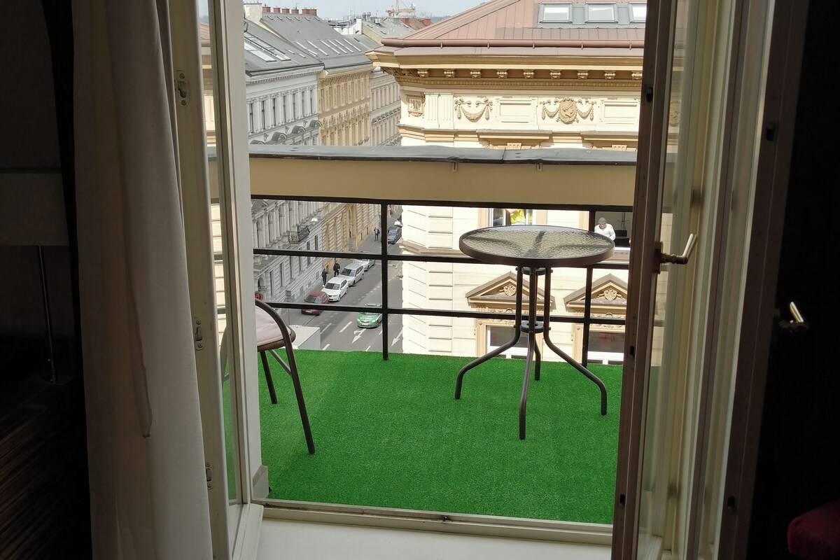 A balcony with a green artificial turf and a metal table and chair.