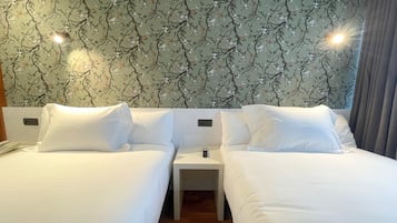 Quarto de hotel com duas camas, uma mesa de cabeceira e papel de parede floral.