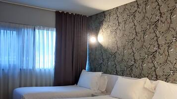 A hotel room with a large bed, a window with curtains, and a wall with a floral pattern.