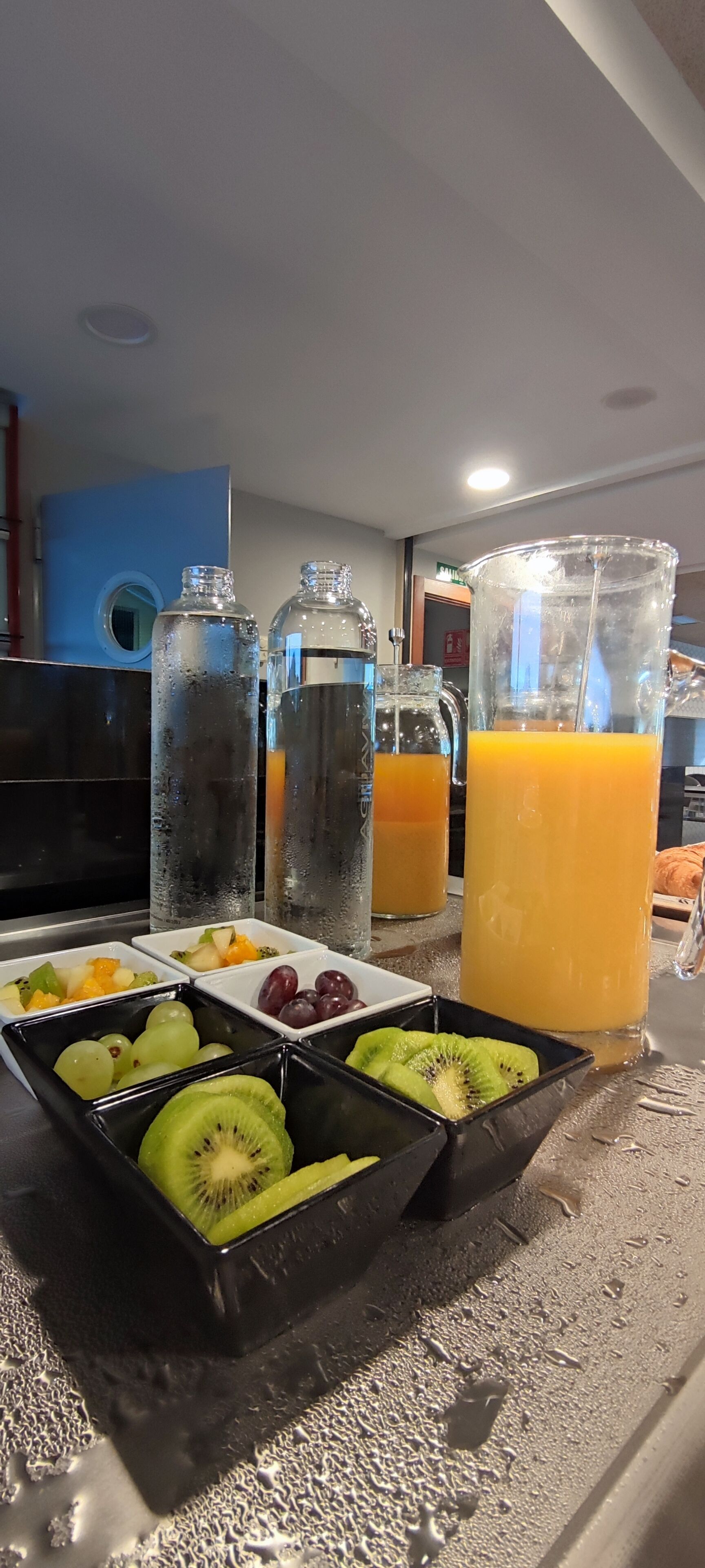 Un buffet de petit-déjeuner avec divers fruits et une grande carafe de jus d’orange.