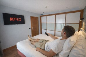 A man lying on a bed in a hotel room with a television displaying the Netflix logo. - Hotel San Fermín Pamplona (Burlada)