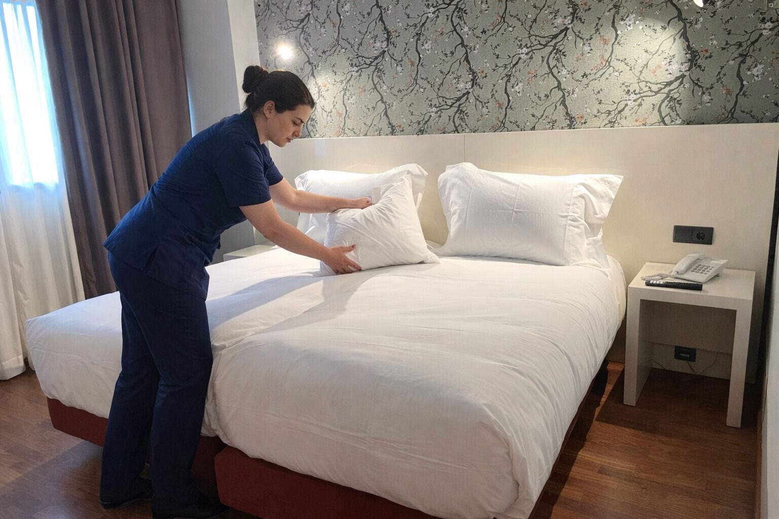 Una habitación de hotel con una cama bien hecha, una mesita de noche con un teléfono y un control remoto, y un papel tapiz floral en la pared.