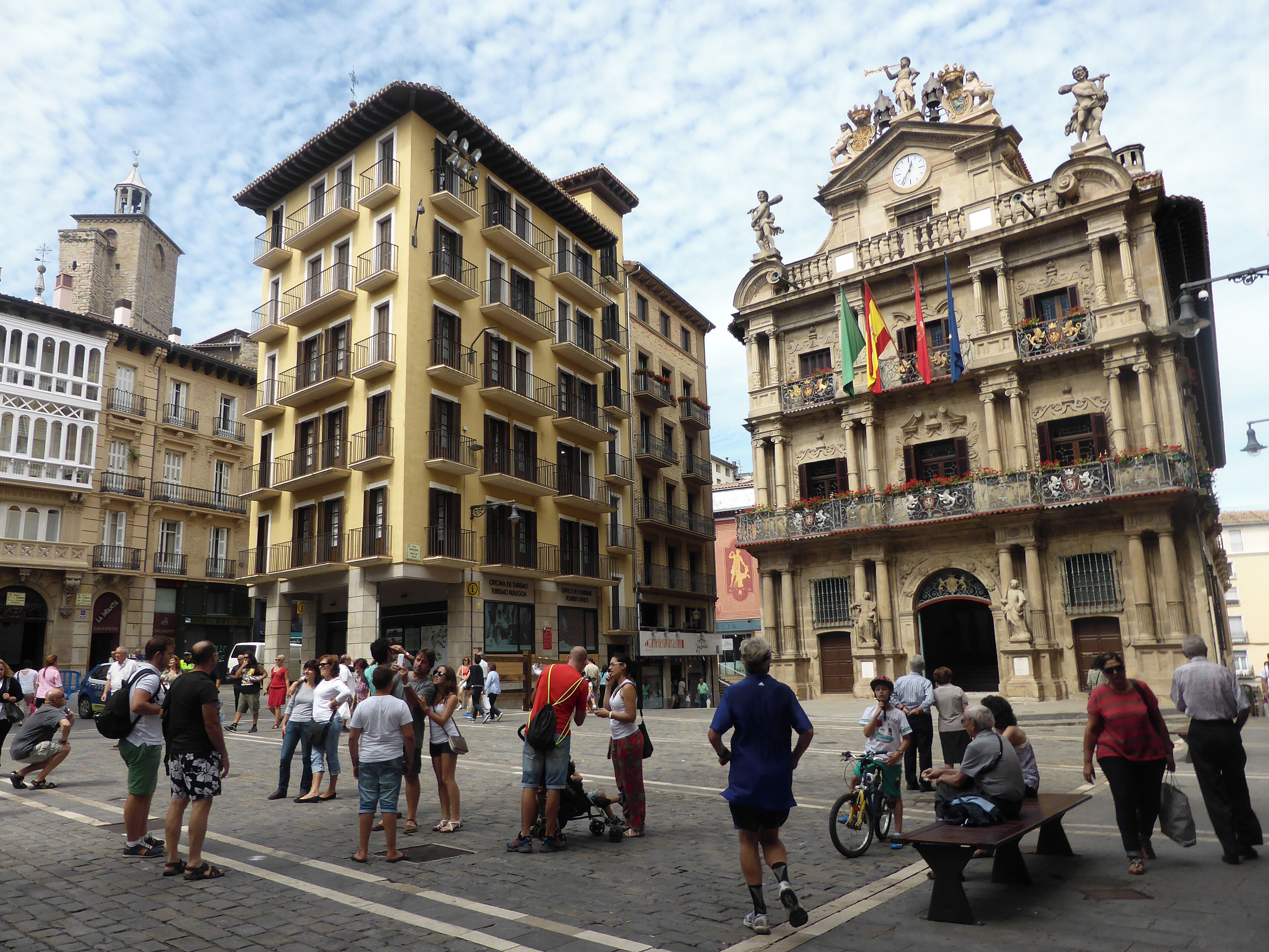 Una plaza animada con edificios históricos, incluyendo un edificio destacado con estatuas y banderas.