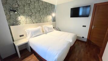 Quarto de hotel com uma cama grande, mesa de cabeceira, televisão presa na parede e chão de madeira.