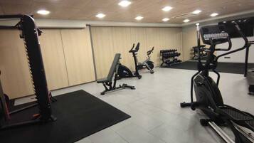 Un gimnasio con máquinas de cardio, equipo de levantamiento de pesas y un espejo grande.