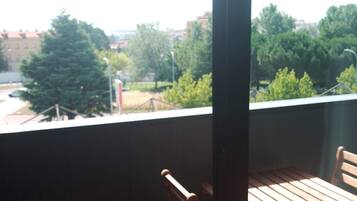 Un balcón con una mesa y sillas de madera, que da a una vista urbana con árboles y edificios.