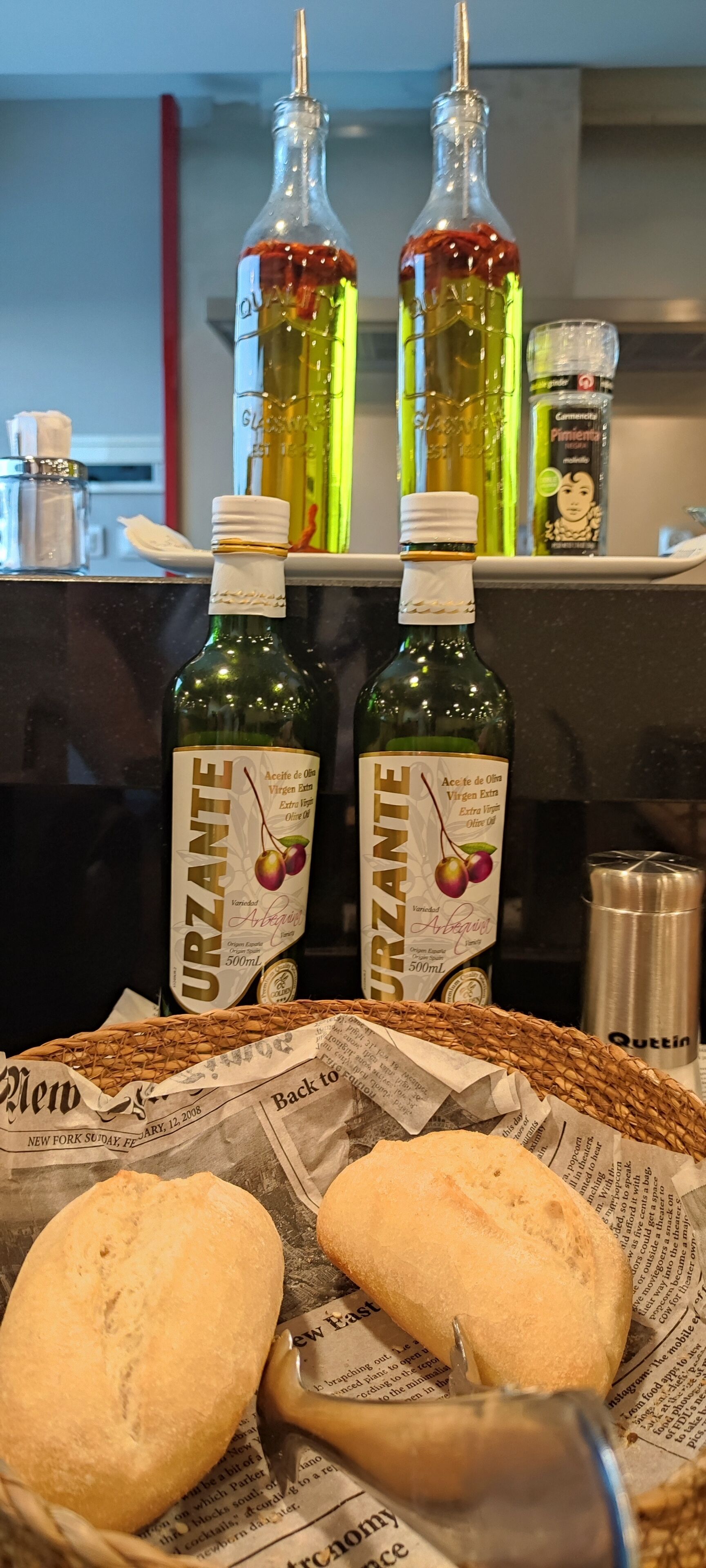 A kitchen counter with two bottles of olive oil, a jar of spice, and a basket with bread.
