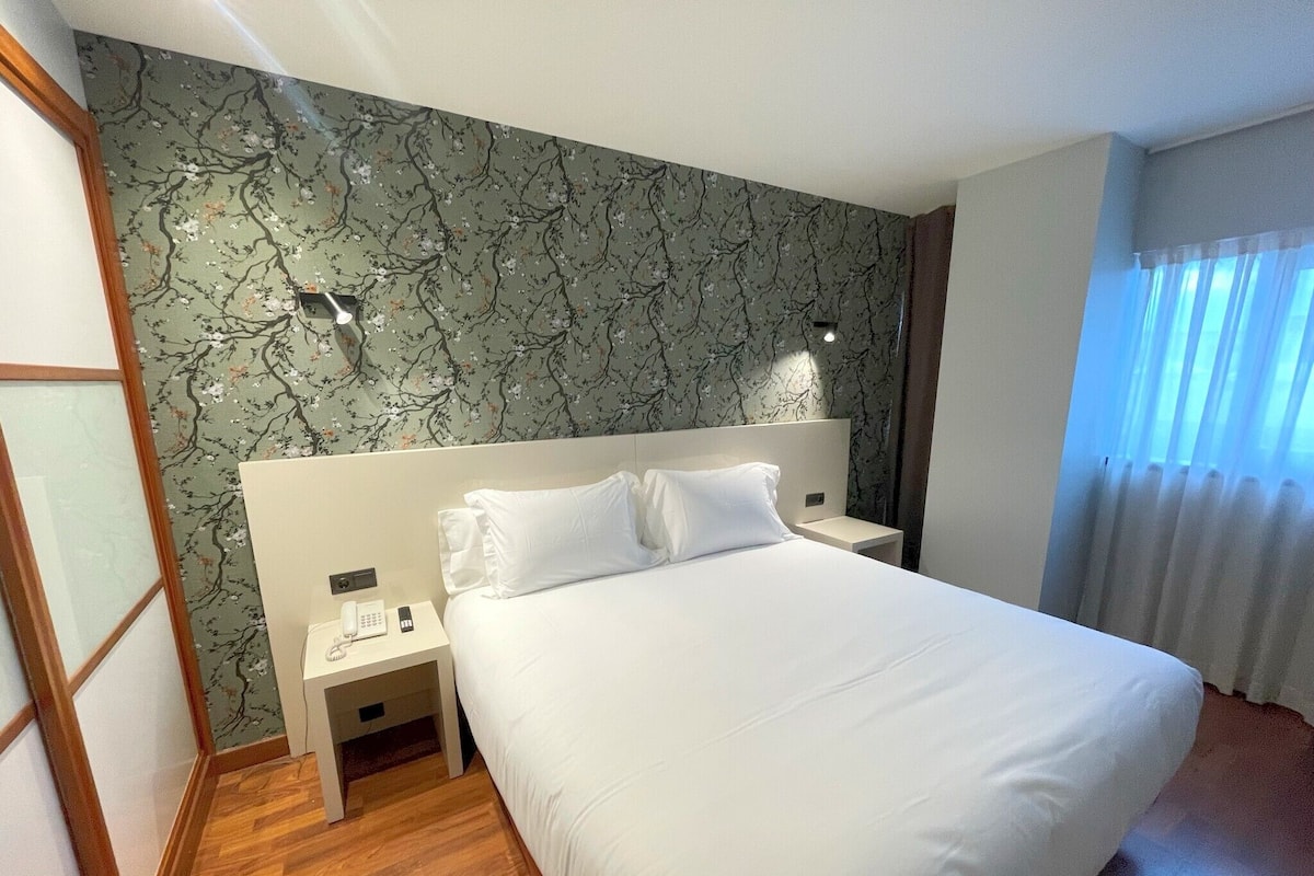 Habitación de hotel con una cama grande, una mesita de noche, un teléfono y una pared con estampado floral.