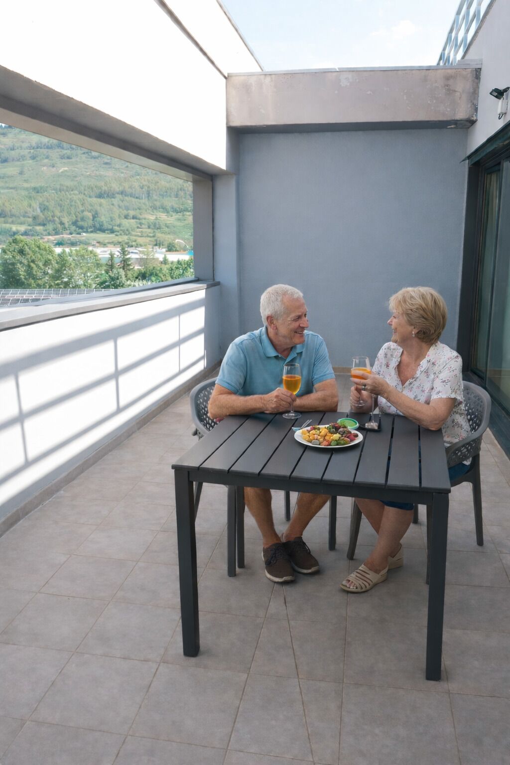 Two people seated at a table on a balcony with a view of a green landscape.
