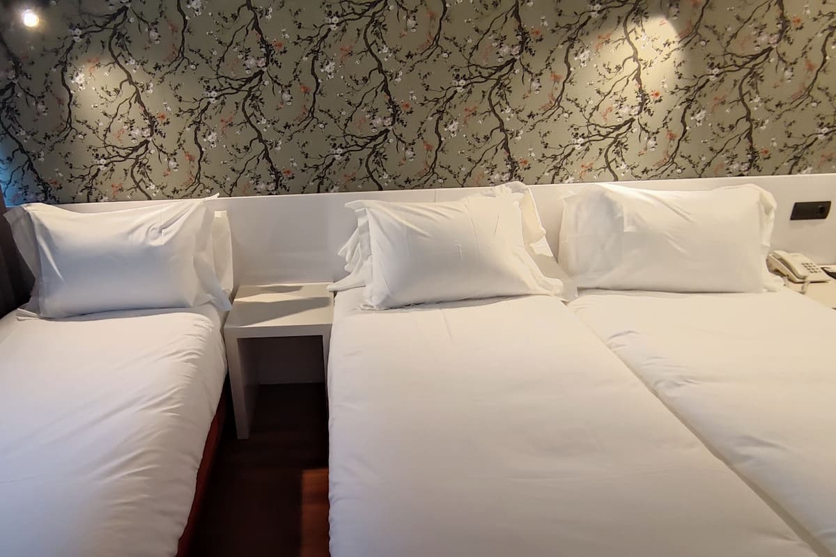 Habitación de hotel con dos camas individuales, una mesita de noche con teléfono y papel tapiz floral.