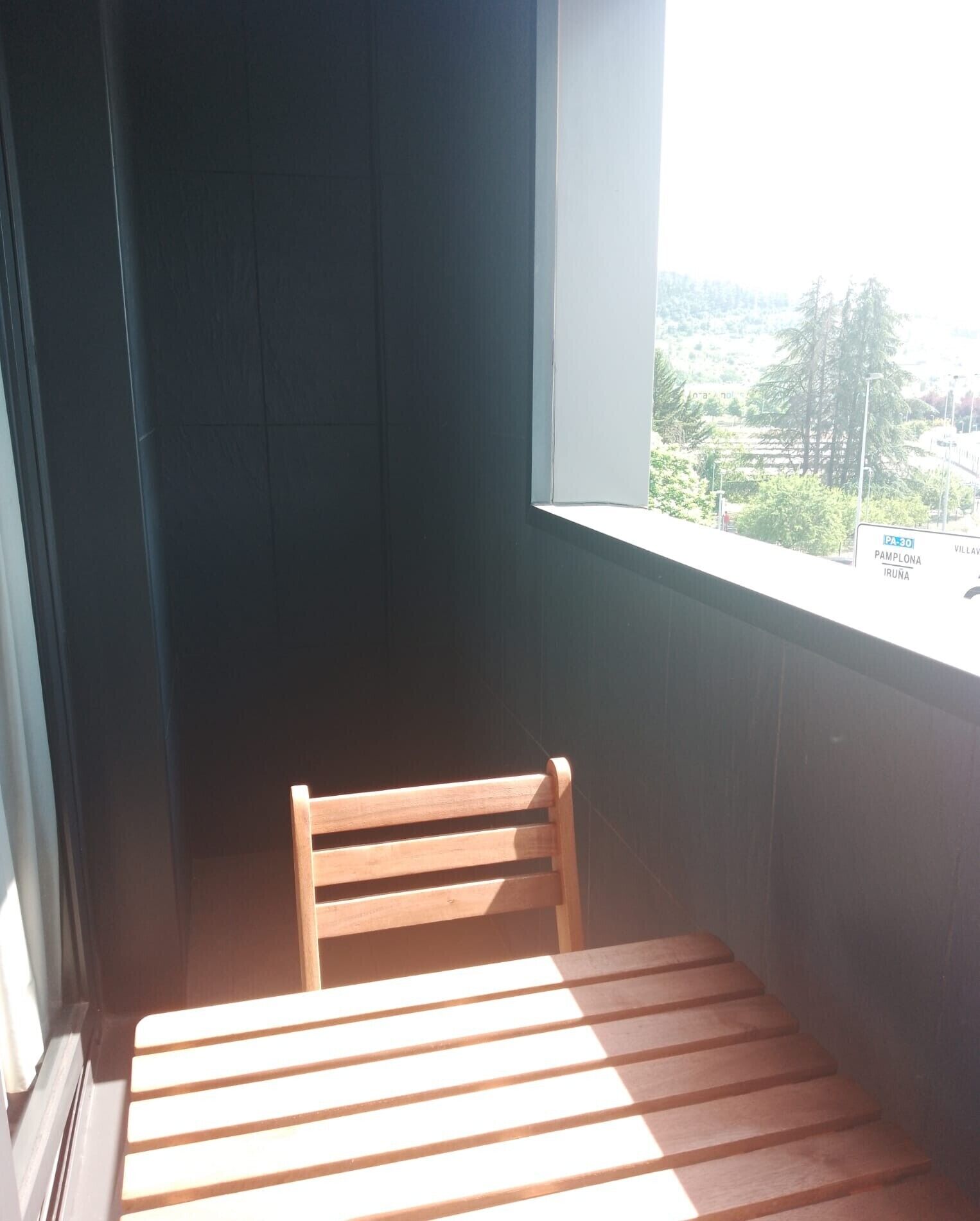 Esquina de una habitación con una silla de madera y una ventana con vistas a la carretera.