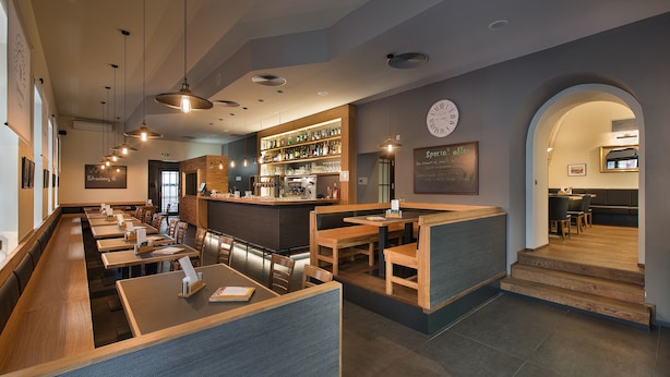 A modern restaurant interior with wooden tables, booths, and a bar area. - EA Hotel Royal Esprit (Prague)
