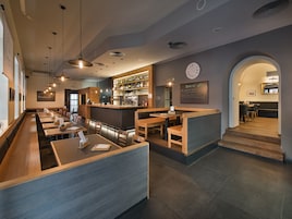 Et moderne restaurantmiljø med træborde, borde med siddepladser og et barområde.