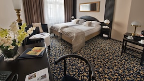 A hotel room with two beds, a desk with a lamp, a chair, a small table with a cup, and a decorative vase with flowers. - EA Hotel Royal Esprit (Prague)