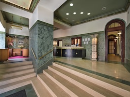 Um hall de entrada com balcão de recepção, escada e área de espera com balcão e cadeiras.