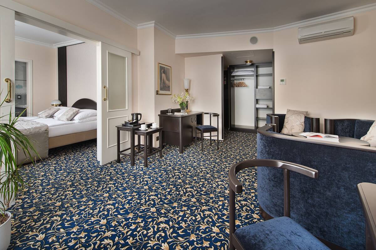 Una habitación de hotel con cama, escritorio, silla, sofá y alfombra estampada.