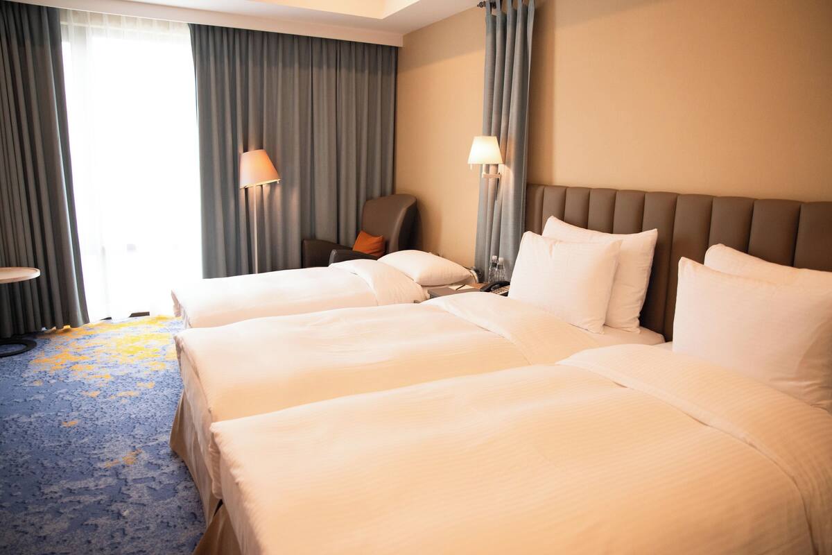 A hotel room with two beds, a chair, and a lamp.