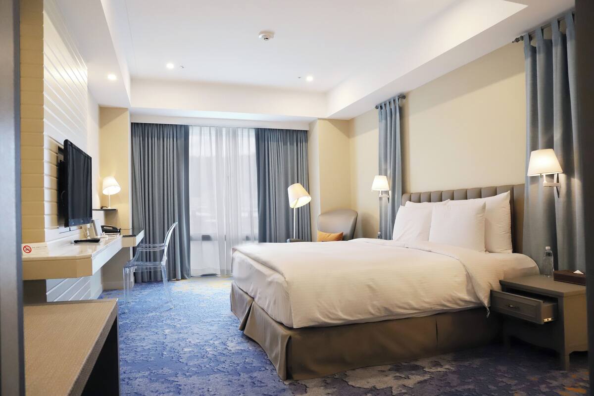 A hotel room with a bed, bedside tables, a desk, a chair, and a television.