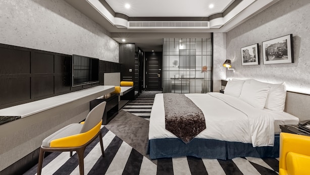 Una habitación de hotel moderna con cama, escritorio, silla, televisor y lámpara.