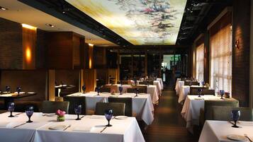 A restaurant with multiple tables set for dining, featuring a ceiling mural and brick walls.
