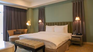 A hotel room with a large bed, a bedside table, a chair, and a window with curtains.