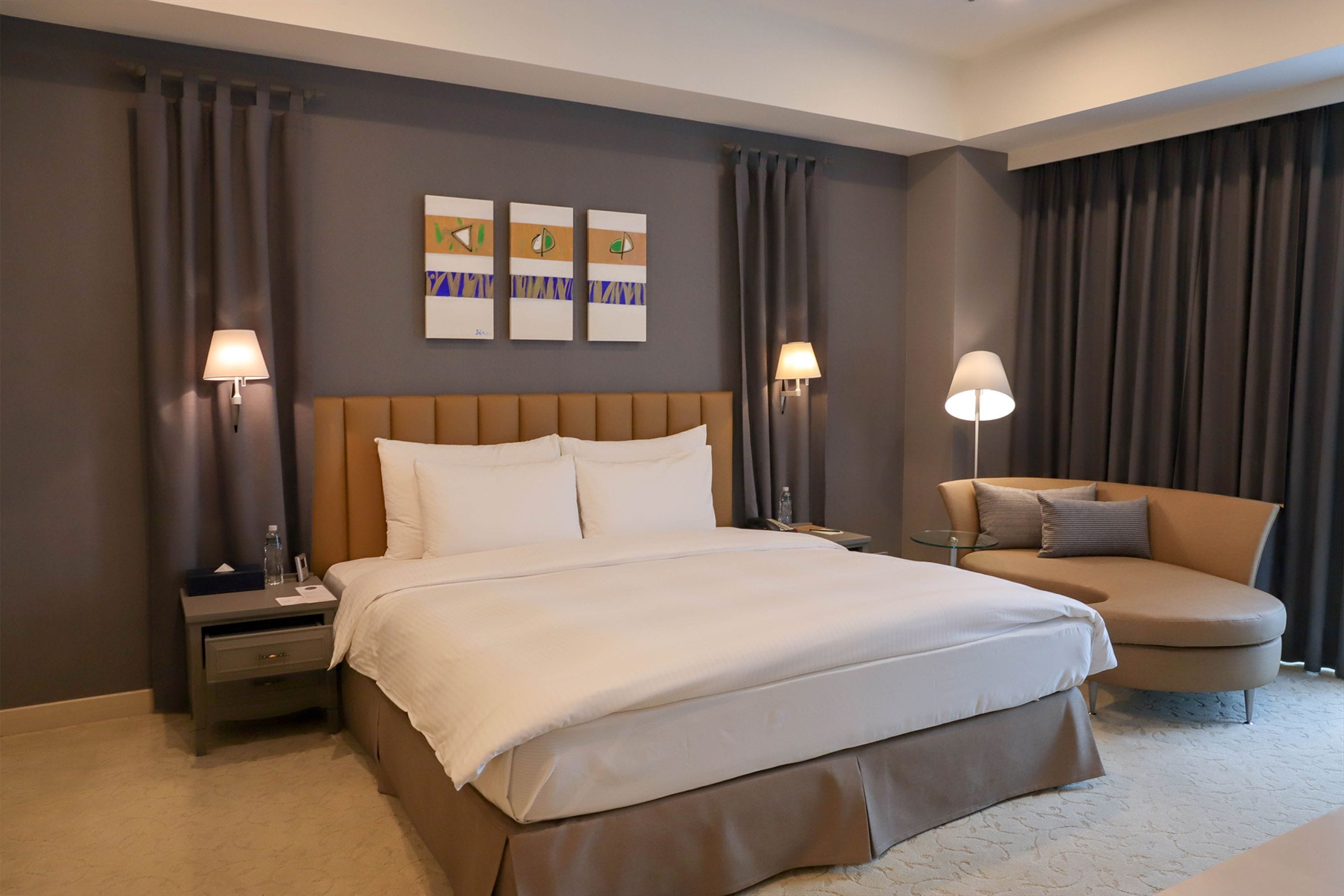 A hotel room with a large bed, two bedside tables, a chair, and artwork on the wall.