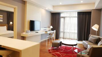 A modern hotel room with a bed, a desk with a computer, a TV, a sofa, and a dining area.