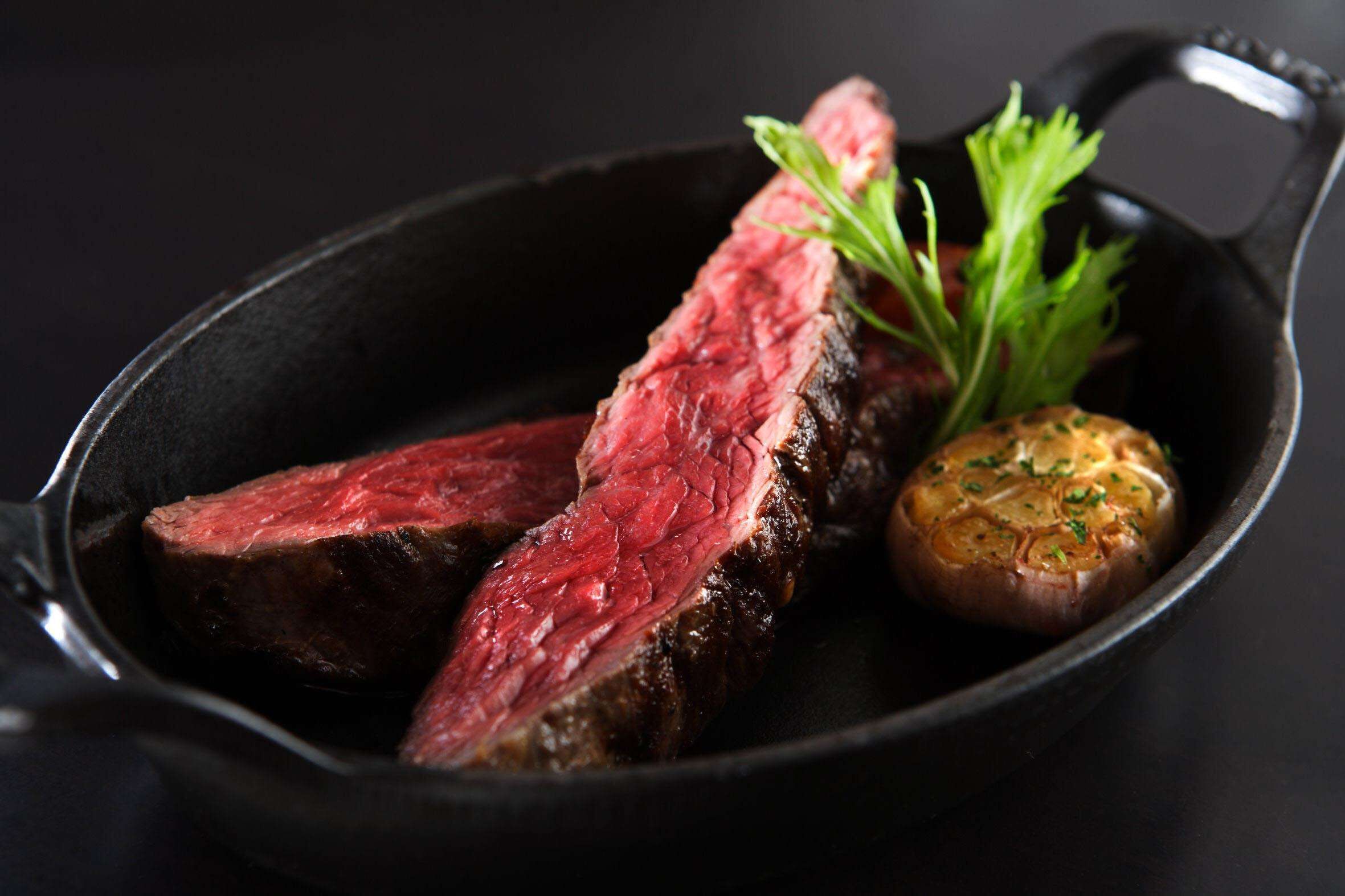 A cast iron skillet with sliced steak and a roasted garlic bulb.