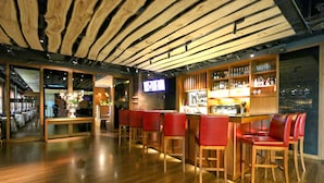 Una zona de bar con suelo de madera, taburetes rojos y un televisor montado en la pared.