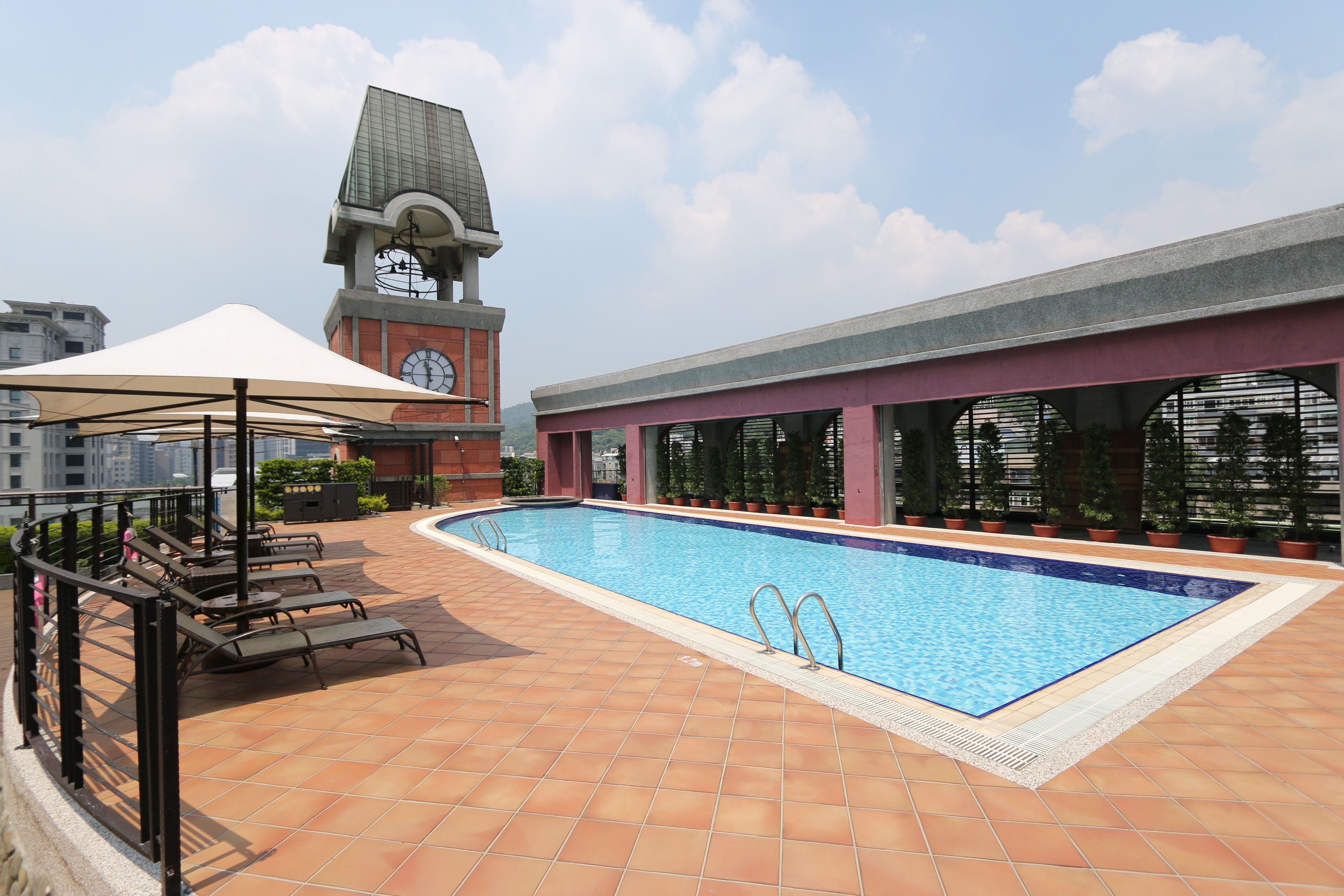 A rooftop pool with lounge chairs and a clock tower in the background.