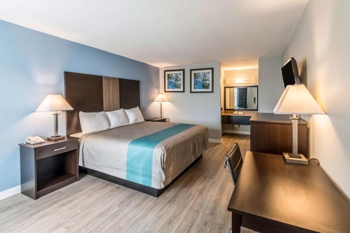 Una habitación de hotel moderna con cama, mesitas de noche, escritorio y espejo.