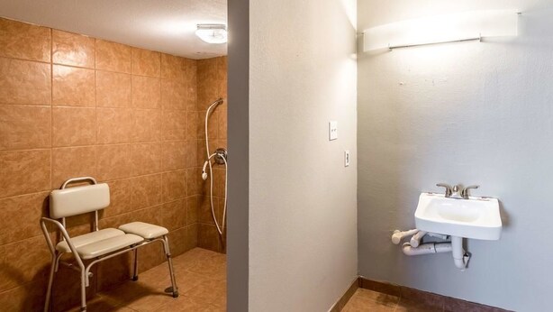 A bathroom with a shower, a sink, and a wheelchair-accessible bench.