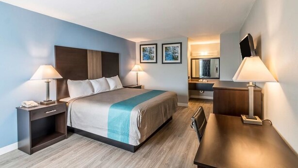 A modern hotel room with a bed, bedside tables, a desk, and a mirror. - Econo Lodge Mineral Wells (Mineral Wells)