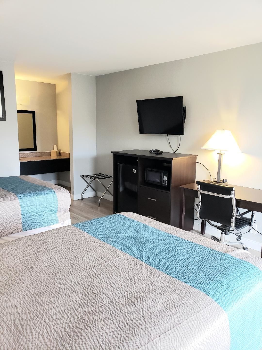 A hotel room with two beds, a desk, a chair, a TV, and a lamp.