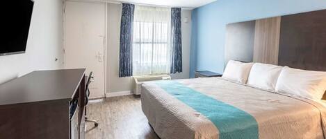 Habitación de hotel con cama, escritorio, televisor, ventana con cortinas y puerta.