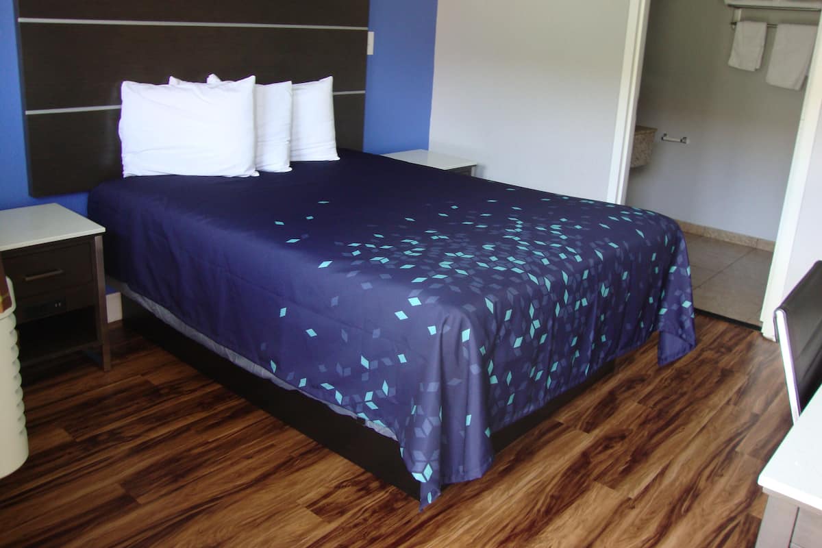A neatly made bed with a dark blue bedspread and white pillows in a room with wooden flooring and blue walls.