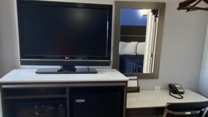 Ett kompakt kontorsutrymme med ett skrivbord, en platt-TV, ett litet kylskåp, en stol och en telefon.