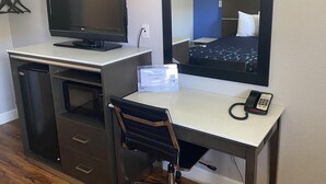 Ett hotellrum med ett skrivbord, en dator, en telefon och en spegel som reflekterar en säng.