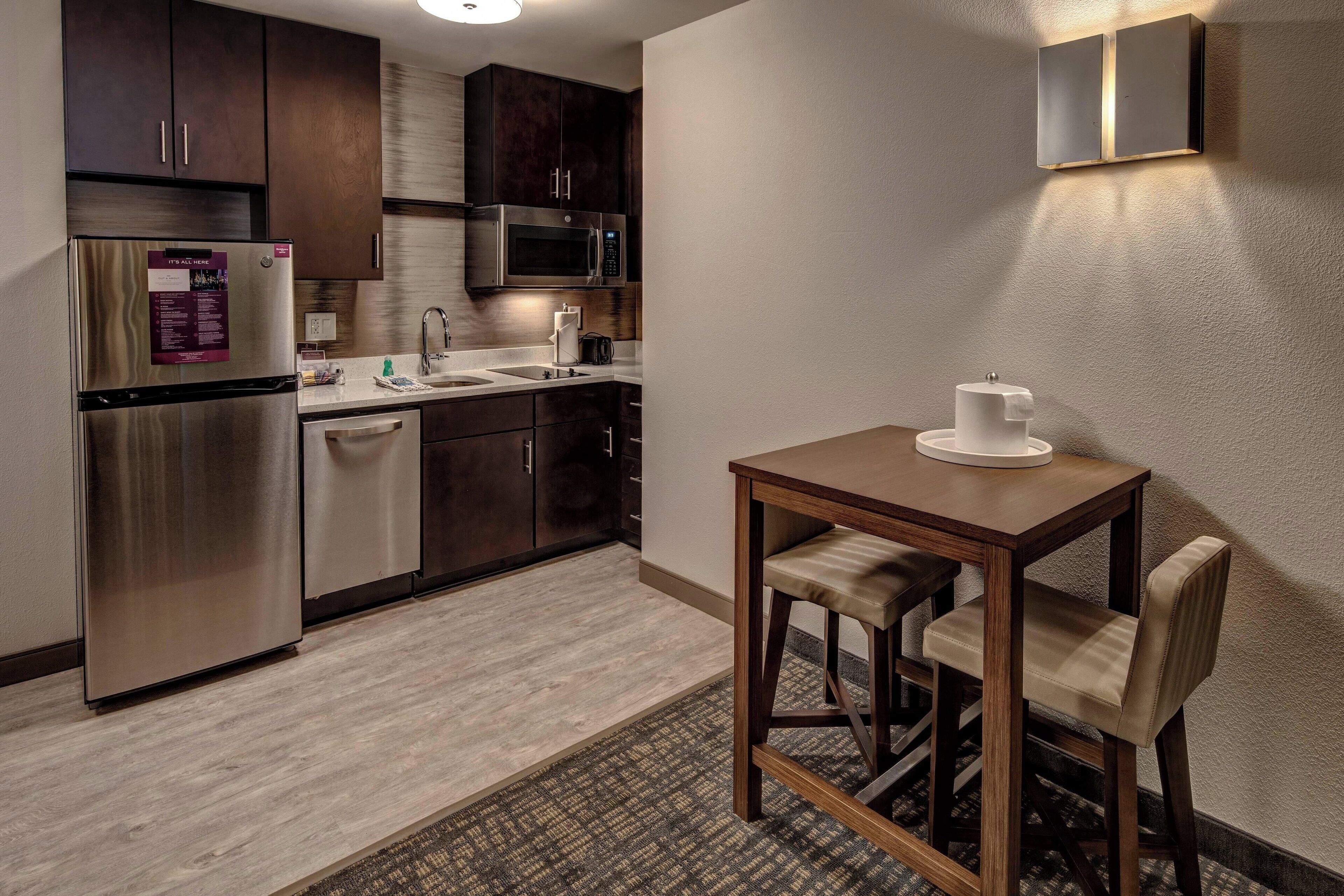 Cocina compacta con armarios de madera oscura, electrodomésticos de acero inoxidable y una pequeña mesa de comedor con dos sillas.